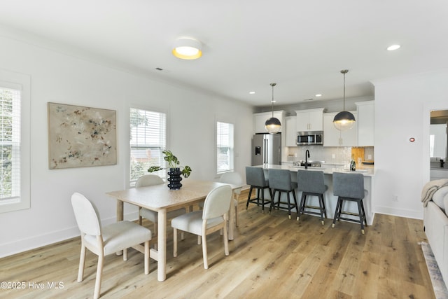 dining room with crown molding, sink, and light hardwood / wood-style flooring