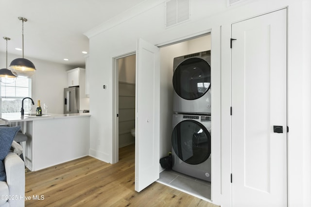 clothes washing area featuring stacked washer / drying machine, light hardwood / wood-style floors, and sink