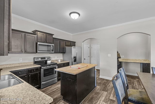 kitchen with wooden counters, dark wood-type flooring, a center island, ornamental molding, and stainless steel appliances