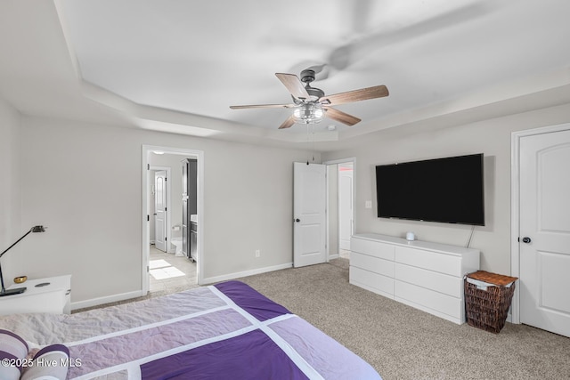 bedroom featuring ceiling fan, ensuite bathroom, light carpet, and a raised ceiling