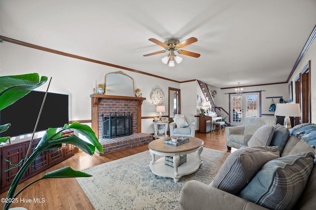 living room with hardwood / wood-style floors, ceiling fan with notable chandelier, a brick fireplace, and ornamental molding