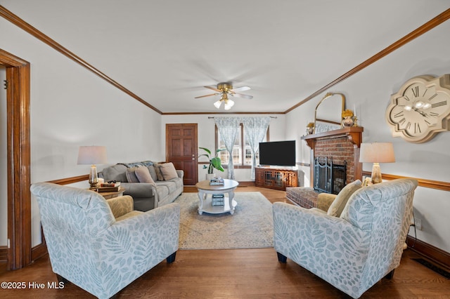 living room with ceiling fan, crown molding, wood-type flooring, and a brick fireplace