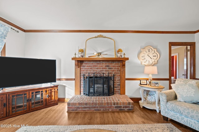 living room with a brick fireplace, ceiling fan, hardwood / wood-style floors, and ornamental molding