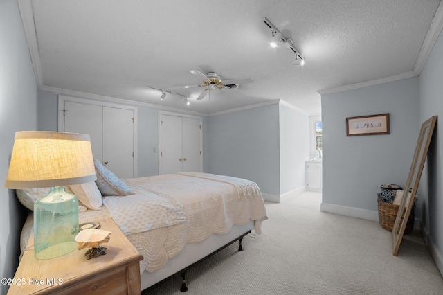 carpeted bedroom with two closets, rail lighting, crown molding, ceiling fan, and a textured ceiling