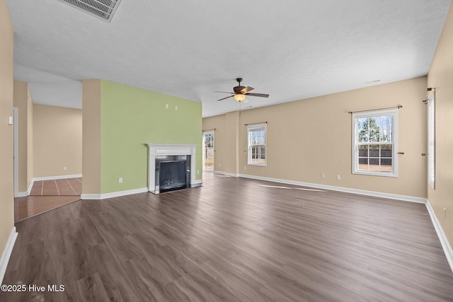 unfurnished living room with a textured ceiling, dark wood-type flooring, ceiling fan, and plenty of natural light