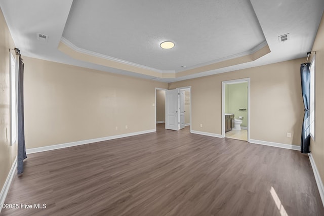 unfurnished bedroom with connected bathroom, a tray ceiling, ornamental molding, and hardwood / wood-style flooring