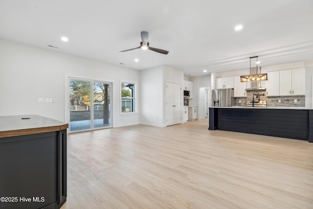 kitchen featuring decorative light fixtures, light hardwood / wood-style flooring, appliances with stainless steel finishes, decorative backsplash, and white cabinets