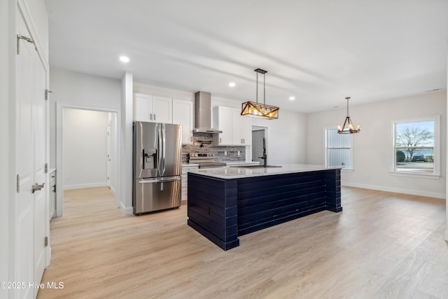 kitchen with wall chimney range hood, sink, appliances with stainless steel finishes, white cabinetry, and an island with sink