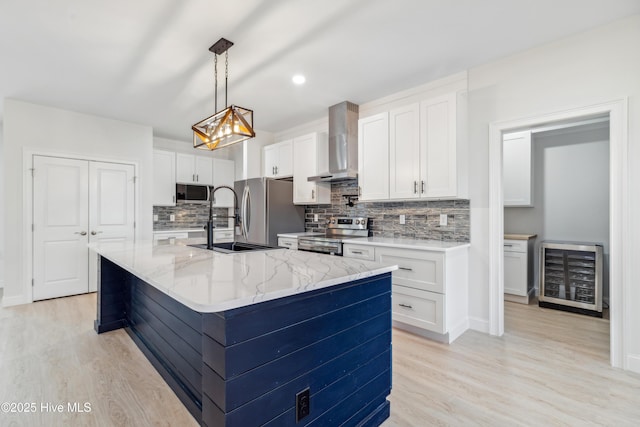 kitchen featuring white cabinets, beverage cooler, wall chimney range hood, stainless steel appliances, and a center island with sink