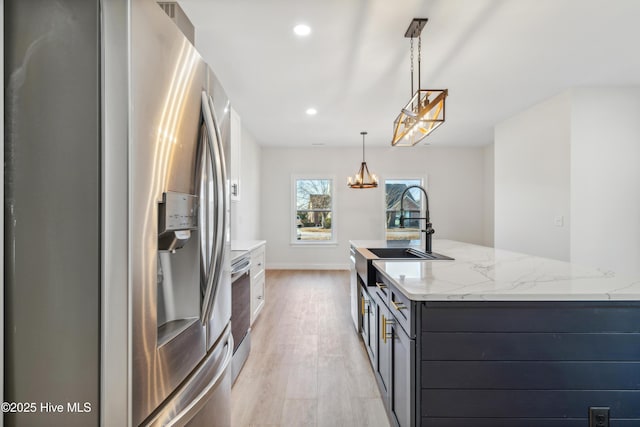 kitchen featuring appliances with stainless steel finishes, pendant lighting, sink, light stone countertops, and light wood-type flooring