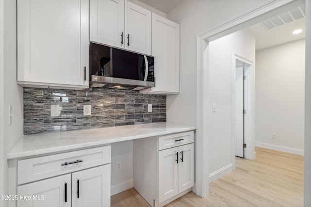 kitchen featuring tasteful backsplash, built in desk, white cabinets, and light hardwood / wood-style flooring