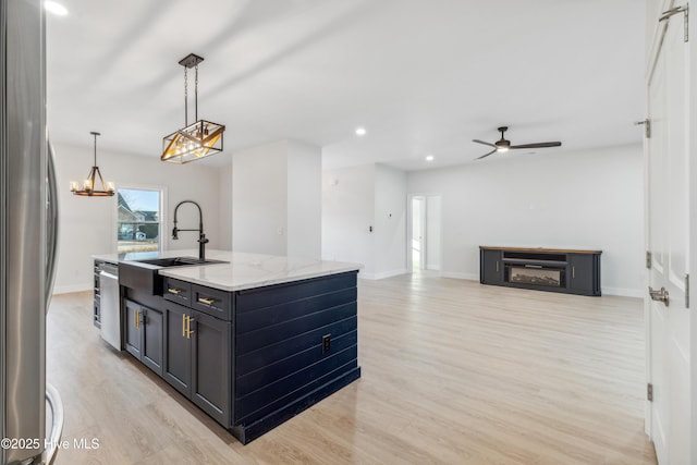 kitchen with light stone counters, a kitchen island with sink, hanging light fixtures, and light hardwood / wood-style flooring