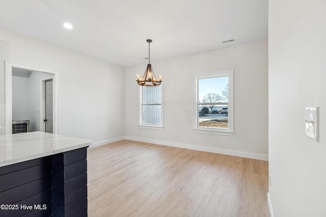 unfurnished dining area featuring an inviting chandelier and light hardwood / wood-style flooring