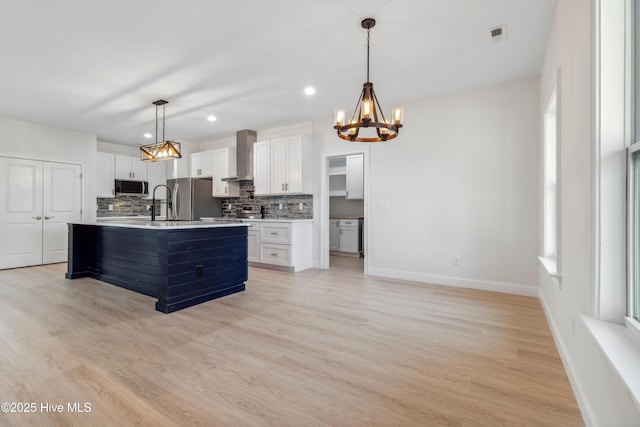 kitchen with appliances with stainless steel finishes, a center island with sink, white cabinets, and wall chimney exhaust hood