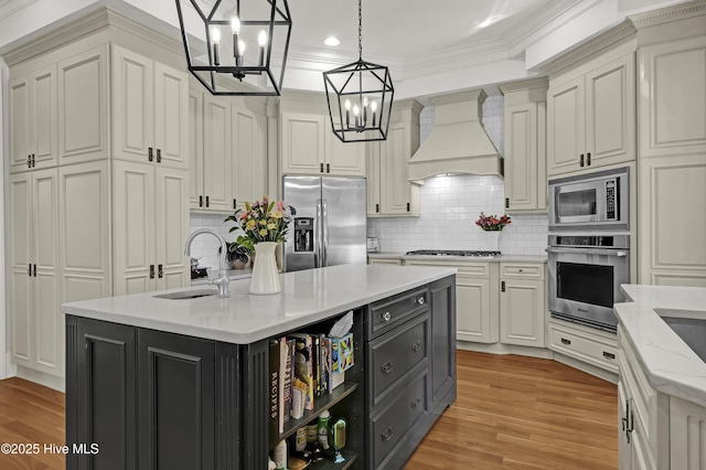 kitchen with hanging light fixtures, premium range hood, stainless steel appliances, an island with sink, and sink