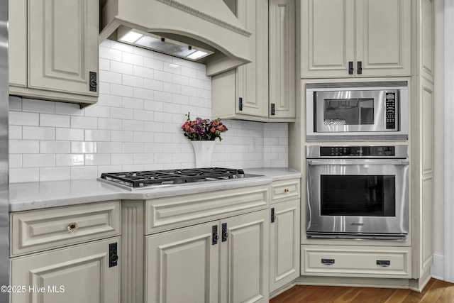 kitchen featuring appliances with stainless steel finishes, light stone countertops, custom range hood, and tasteful backsplash