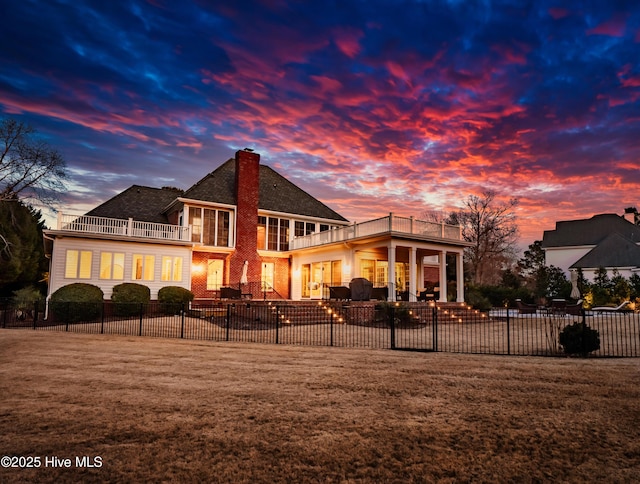 back house at dusk featuring a patio, a yard, and a balcony