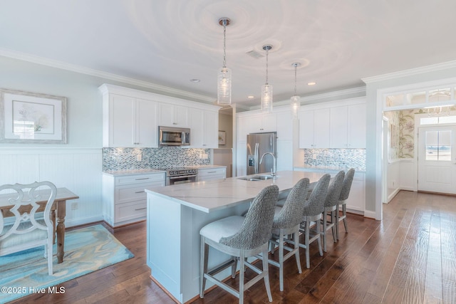 kitchen featuring appliances with stainless steel finishes, pendant lighting, white cabinets, dark hardwood / wood-style flooring, and a kitchen island with sink