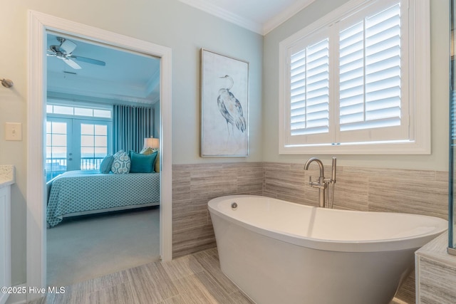 bathroom with french doors, crown molding, tile walls, ceiling fan, and a washtub