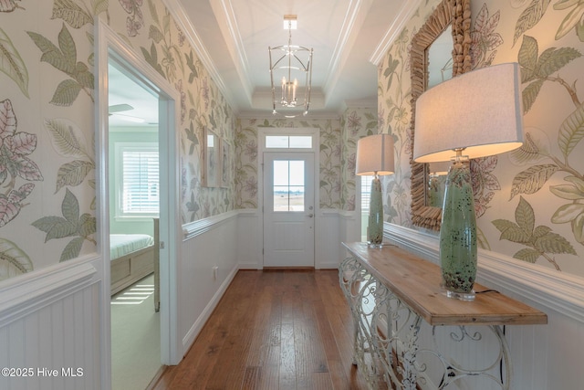 doorway with crown molding, wood-type flooring, a notable chandelier, and a tray ceiling