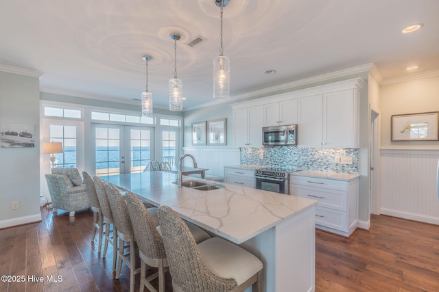 kitchen with sink, stainless steel appliances, a water view, white cabinets, and decorative light fixtures