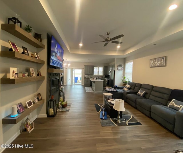 living room featuring a raised ceiling, ceiling fan, and dark hardwood / wood-style floors