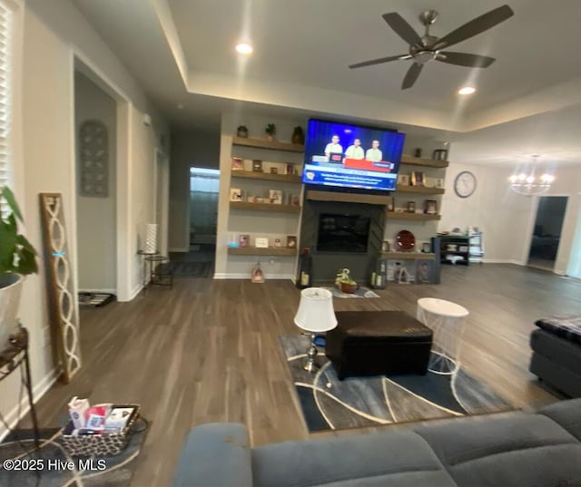 living room with a raised ceiling, wood-type flooring, a fireplace, and ceiling fan with notable chandelier