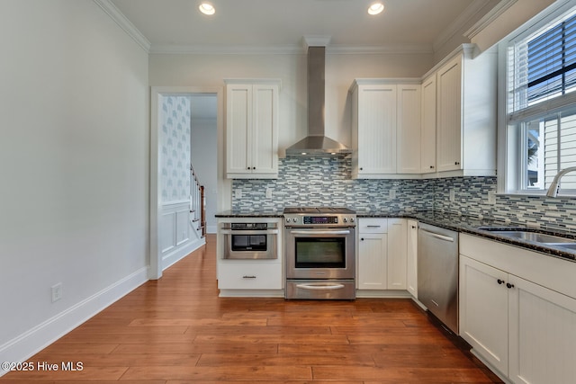 kitchen with wood finished floors, a sink, ornamental molding, appliances with stainless steel finishes, and wall chimney exhaust hood