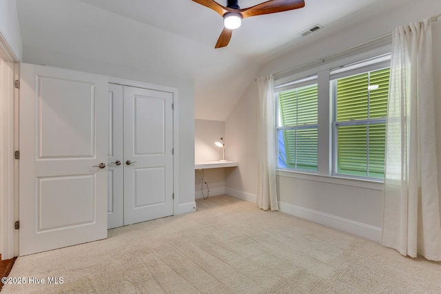 unfurnished bedroom featuring built in desk, vaulted ceiling, ceiling fan, a closet, and light colored carpet