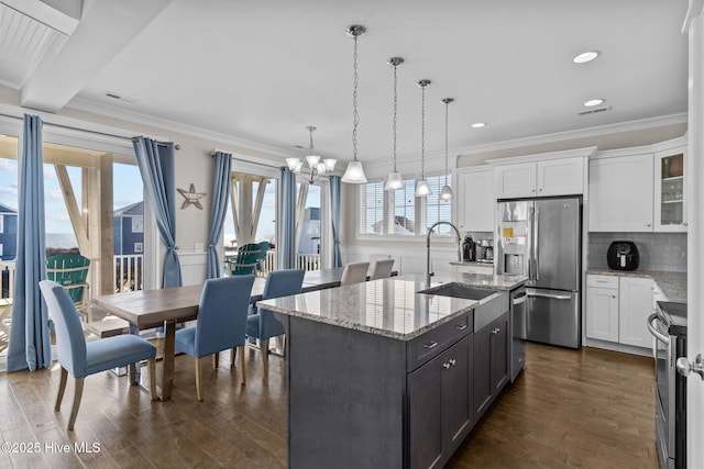 kitchen with appliances with stainless steel finishes, white cabinetry, sink, hanging light fixtures, and a center island with sink