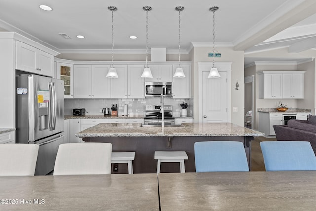 kitchen with a center island with sink, a breakfast bar area, stainless steel appliances, pendant lighting, and white cabinets