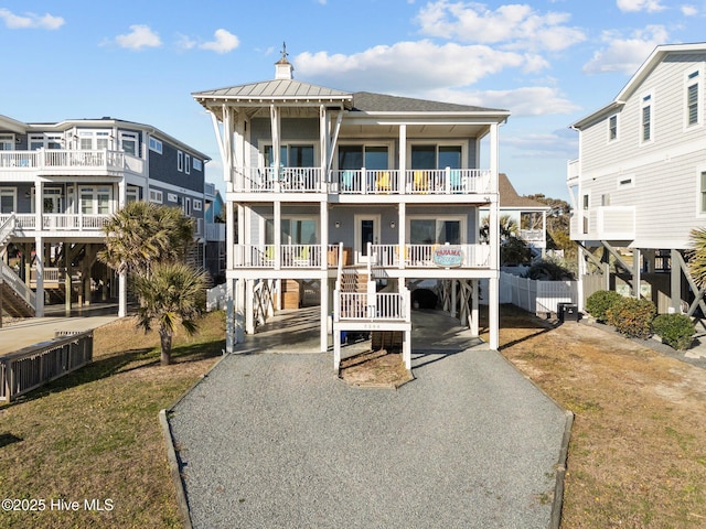 raised beach house with a front lawn, a balcony, a carport, and covered porch