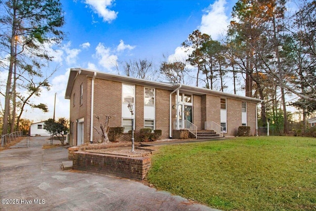 view of front of house with a front yard, brick siding, driveway, and an attached garage