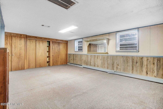 basement with a textured ceiling, wood walls, and baseboard heating