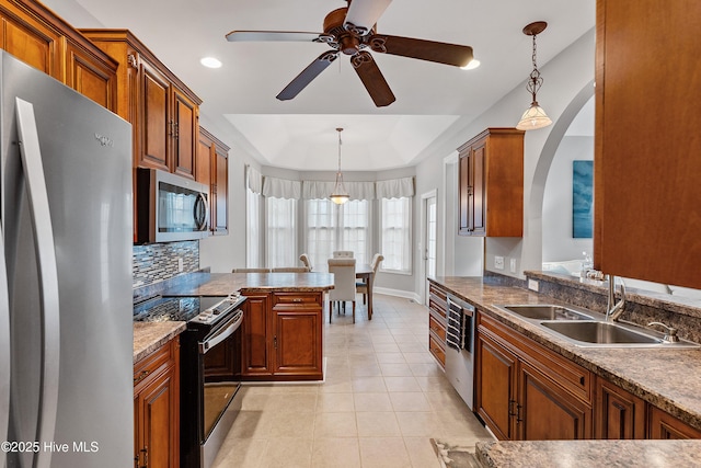 kitchen featuring hanging light fixtures, a tray ceiling, appliances with stainless steel finishes, ceiling fan, and sink