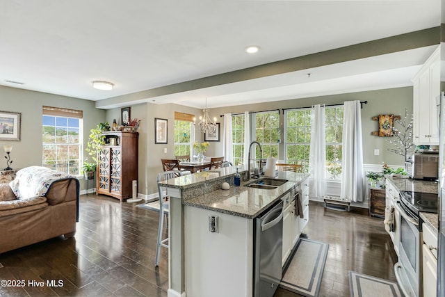 kitchen featuring decorative light fixtures, white cabinetry, stainless steel appliances, sink, and a kitchen island with sink