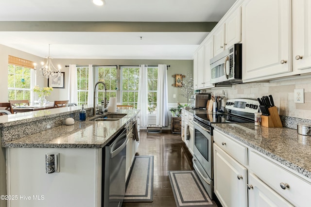 kitchen with an island with sink, stainless steel appliances, a notable chandelier, white cabinets, and sink