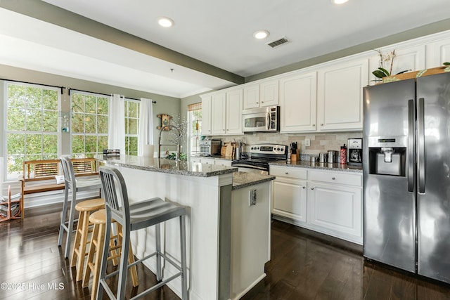 kitchen with dark hardwood / wood-style floors, a center island with sink, white cabinetry, stainless steel appliances, and dark stone counters