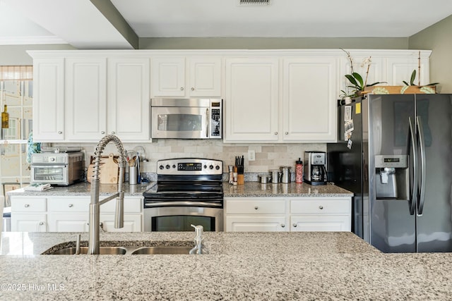 kitchen featuring tasteful backsplash, sink, white cabinetry, light stone countertops, and stainless steel appliances