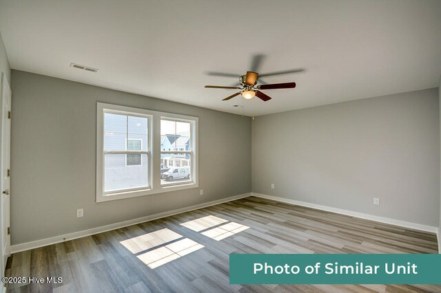 empty room with wood finished floors, a ceiling fan, visible vents, and baseboards