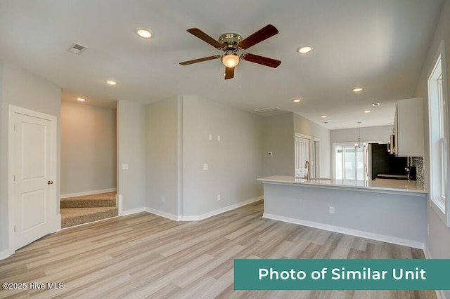 unfurnished living room with ceiling fan with notable chandelier, sink, and light hardwood / wood-style flooring