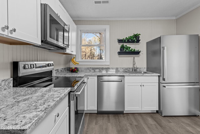 kitchen featuring appliances with stainless steel finishes, light hardwood / wood-style floors, ornamental molding, white cabinets, and sink