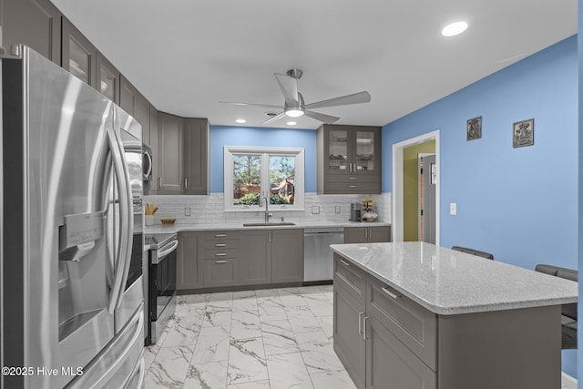 kitchen featuring sink, light stone counters, a kitchen island, decorative backsplash, and stainless steel appliances