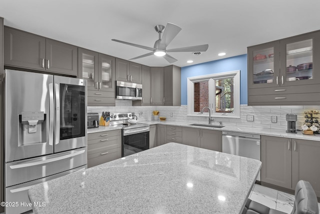 kitchen featuring ceiling fan, appliances with stainless steel finishes, sink, tasteful backsplash, and light stone countertops