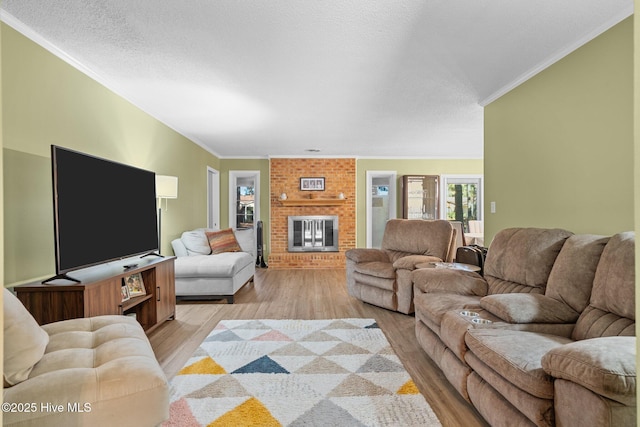 living room featuring a textured ceiling, light hardwood / wood-style flooring, a brick fireplace, and crown molding