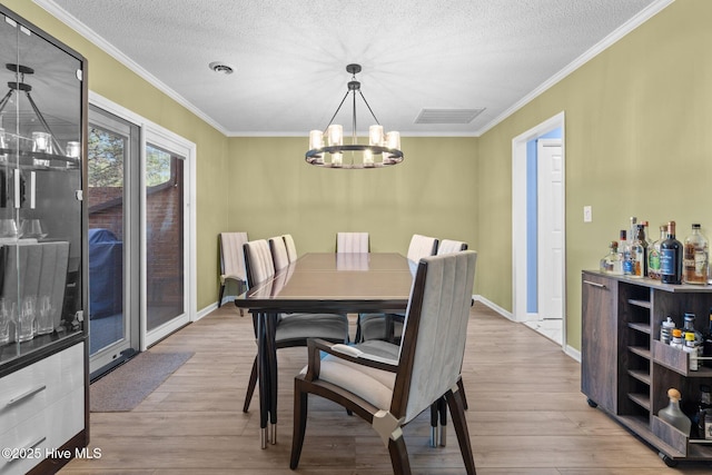 dining room with light hardwood / wood-style floors, a textured ceiling, ornamental molding, and a chandelier