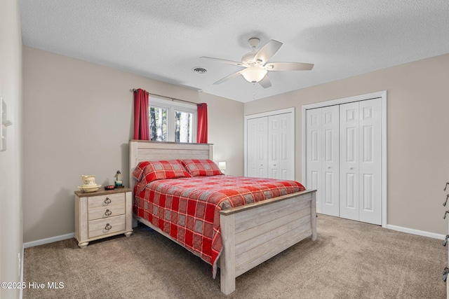 bedroom with ceiling fan, two closets, dark carpet, and a textured ceiling