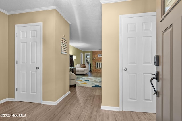 foyer entrance with a textured ceiling, light hardwood / wood-style flooring, crown molding, and a fireplace