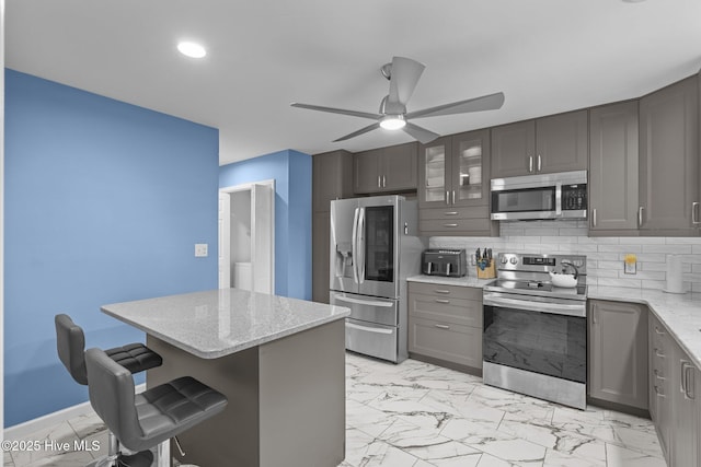 kitchen with light stone counters, tasteful backsplash, a breakfast bar, and appliances with stainless steel finishes