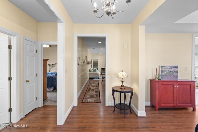 corridor with dark wood-type flooring and a chandelier